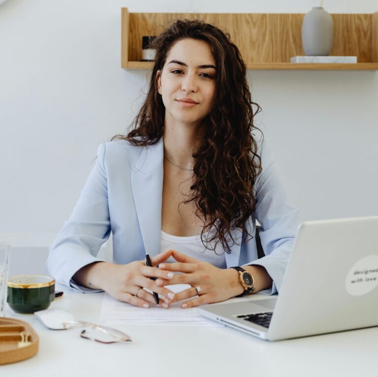 Portrait of a confident businesswoman sitting at a desk with a laptop in a modern office.